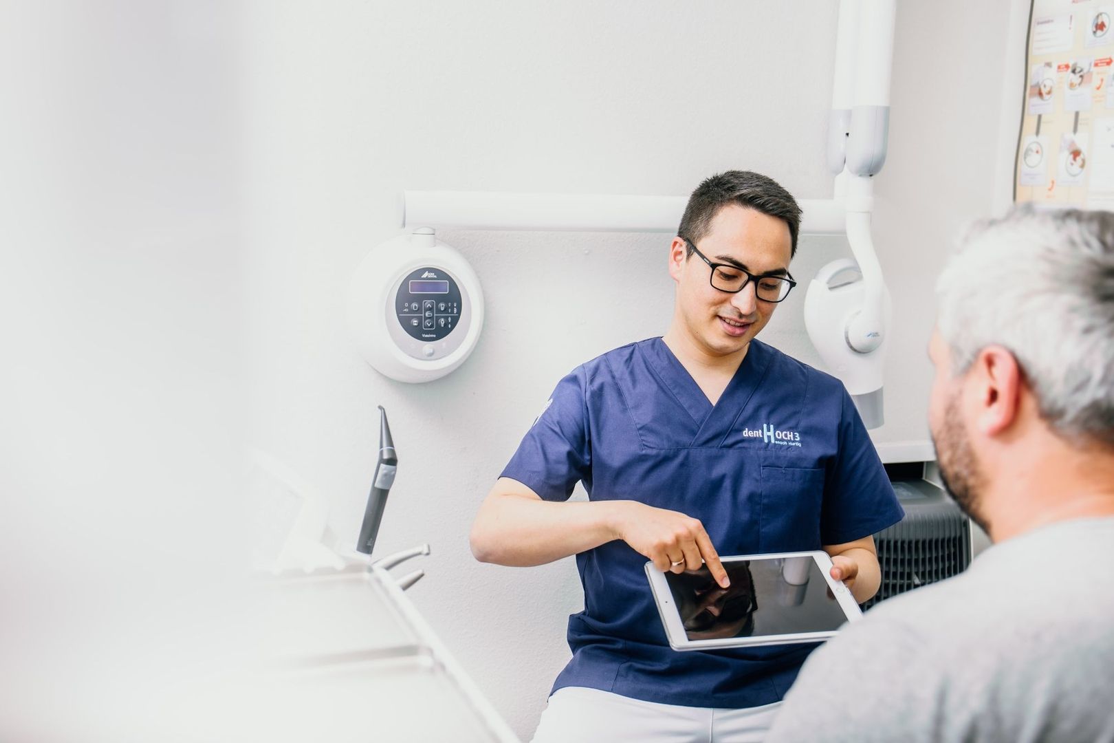 Zahnarzt erklärt einem Patienten im Behandlungszimmer die Befunde auf dem Tablet